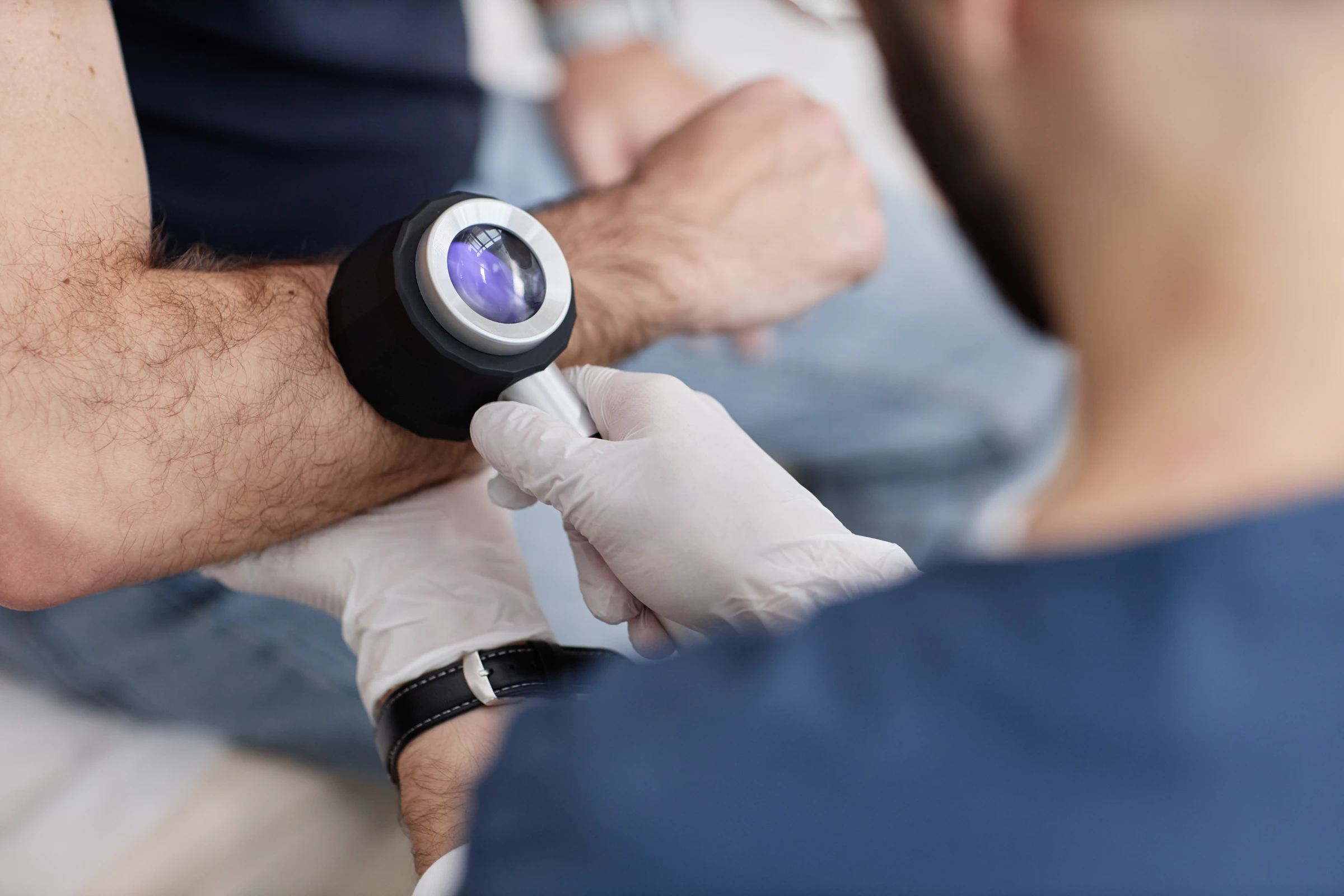 A clinician examining a patient’s arm with a dermatoscope.